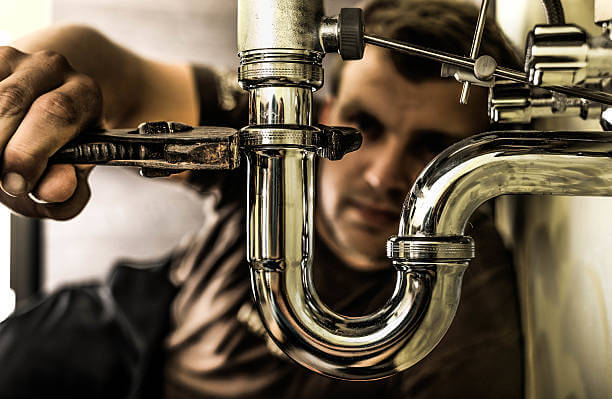 Plumber using a wrench to tighten a siphon under a sink.